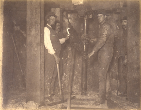 Mt Con 400 level East sill floor breast. Showing Supt. Carroll and drilling machine in act of drilling ore breast